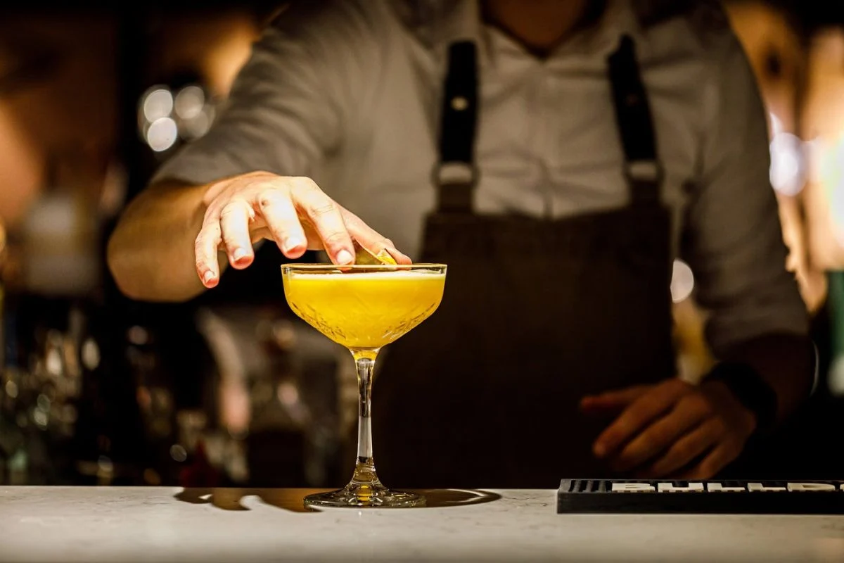 Barman zet een cocktail met citroenschil op de bar