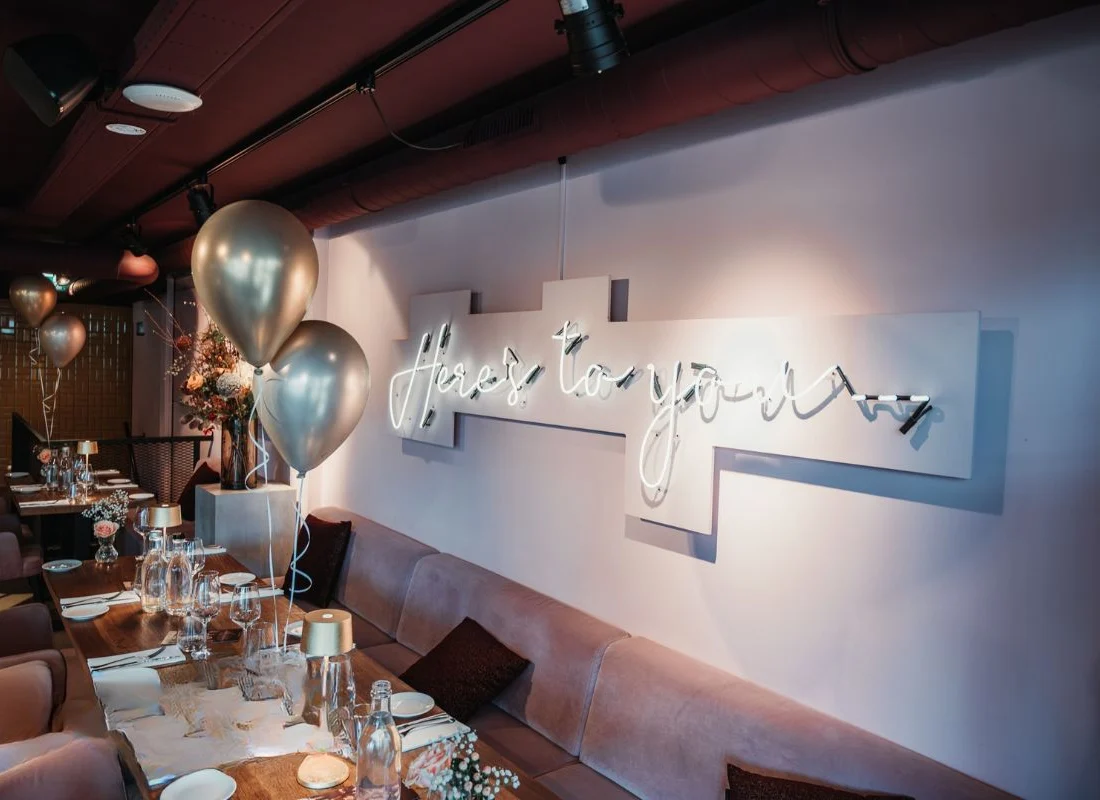 Gedekte tafel met ballonnen onder de neonletters Here's to you